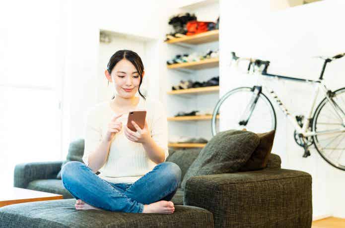 ロードバイクを背に、スマホを触る女性の画像