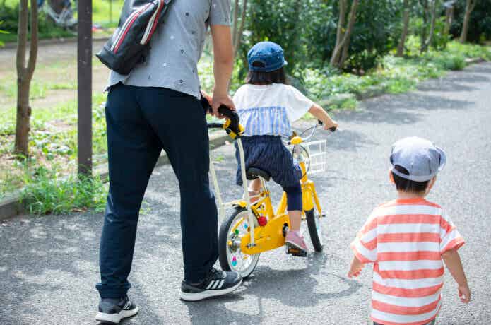 女の子の自転車練習のサポートをする父親