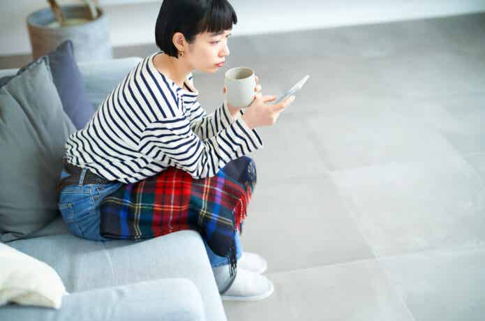 リビングでコーヒーを片手にスマホを見る女性