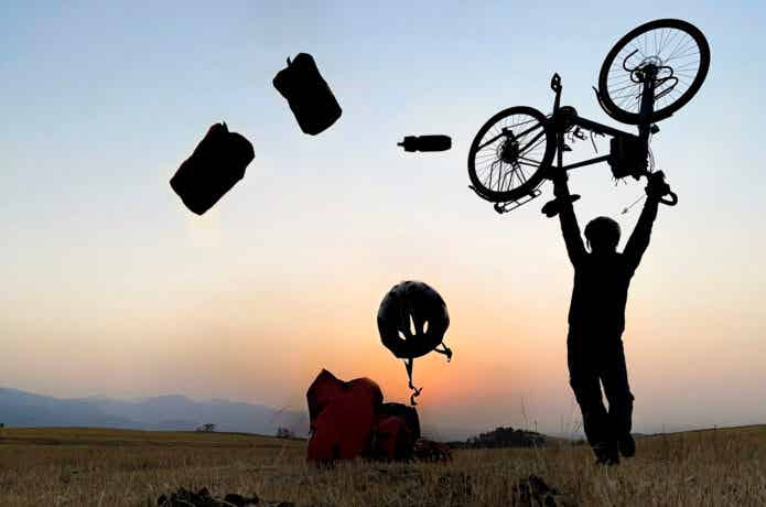 夕日をバッグに自転車を差し上げる男性