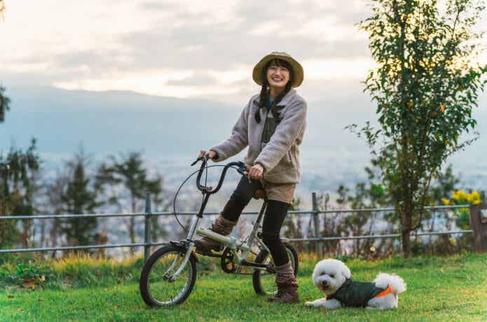 キャンプ場で折りたたみ自転車に乗る女性とそばにいる飼い犬