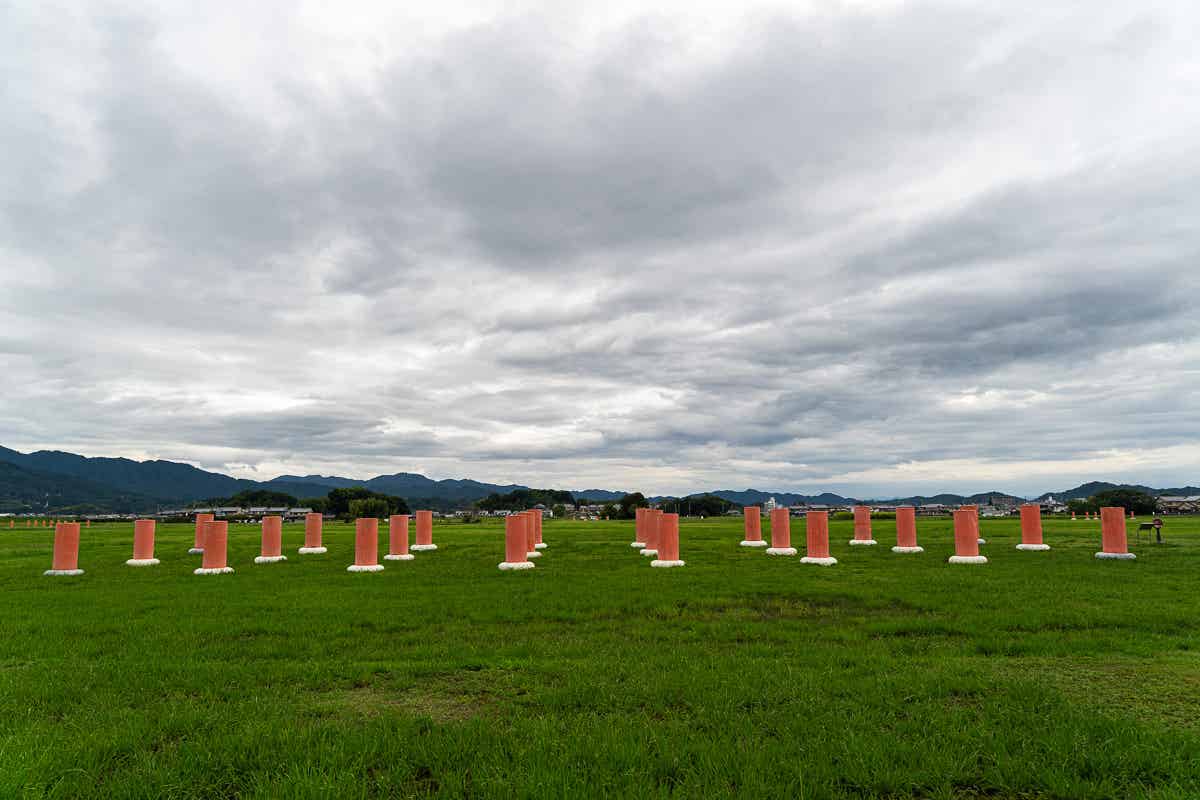 曇り空の下、赤い柱が並ぶ藤原宮跡の広大な原っぱ
